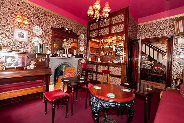 The Victorian-style residential bar with red velvet stools, mahogany and gilt lamps